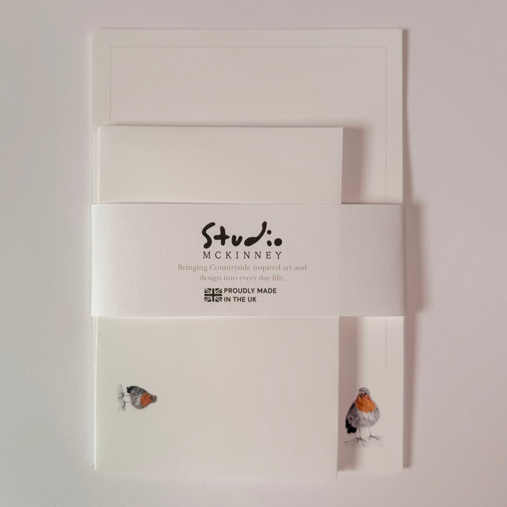 Studio McKinney white stationery set featuring envelopes and cards with a central white paper band printed with the brand name, photographed against a light neutral background.